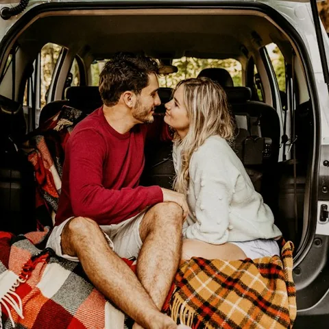 A couple cuddled up in the back of a car under blankets