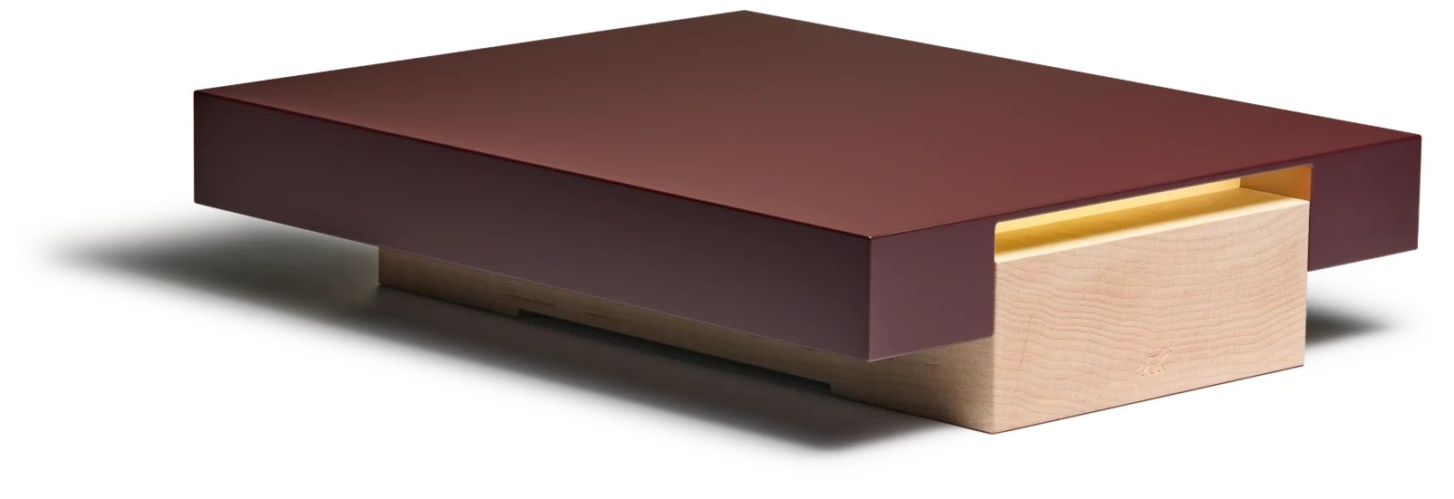 The Vora Aegis appliance at a three-quarter angle: an oxblood aluminum slab above a maple drawer embossed with the Vora badger.