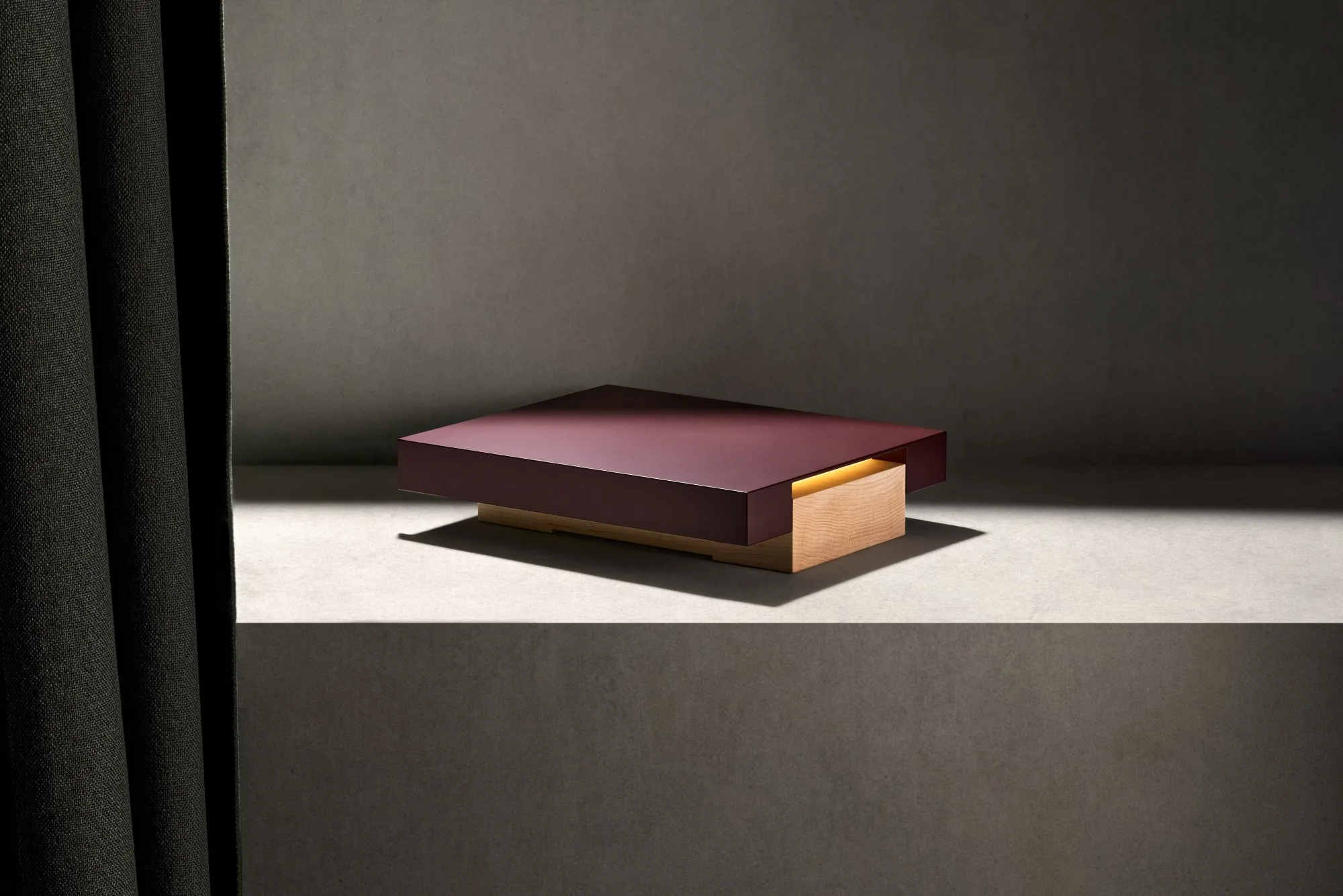 Vora Aegis on a stone shelf beside a dark curtain, a band of daylight across it and the warm line of light glowing under its burgundy top.